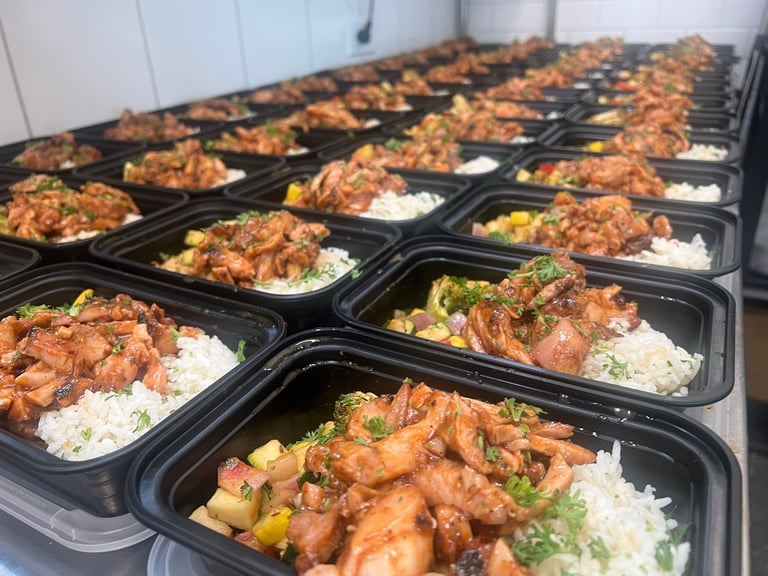 Multiple black meal prep containers filled with caramelized chicken, rice, and vegetables arranged in rows