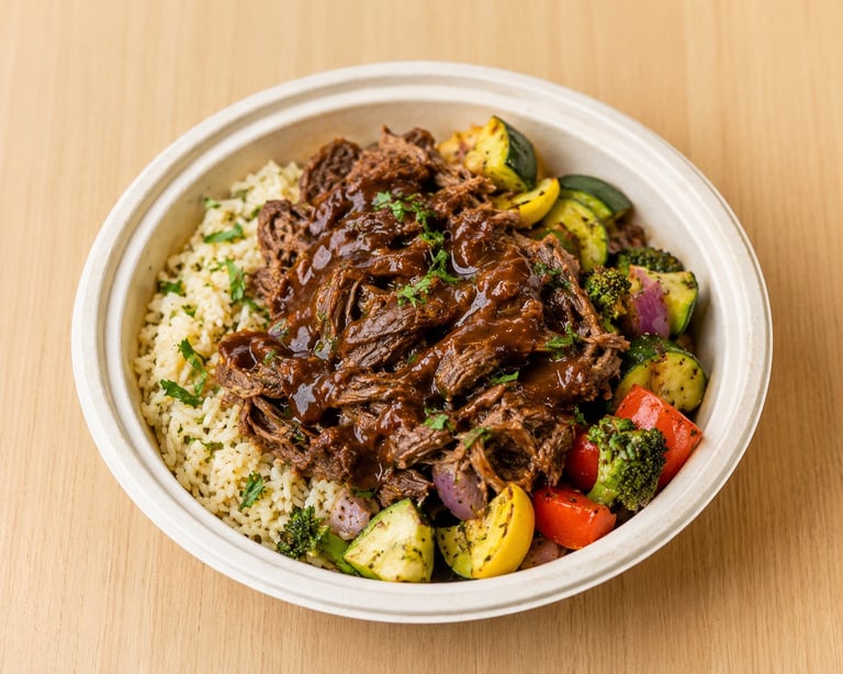 Shredded slow-cooked beef served over cauliflower rice with roasted vegetables in a white bowl