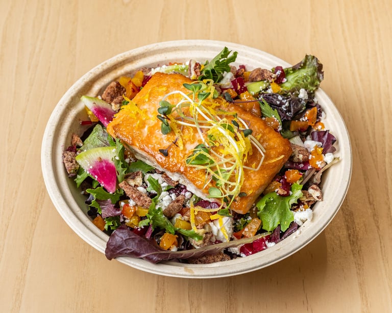 Glazed salmon fillet with julienned garnish on a bed of colorful mixed greens and vegetables in a white bowl