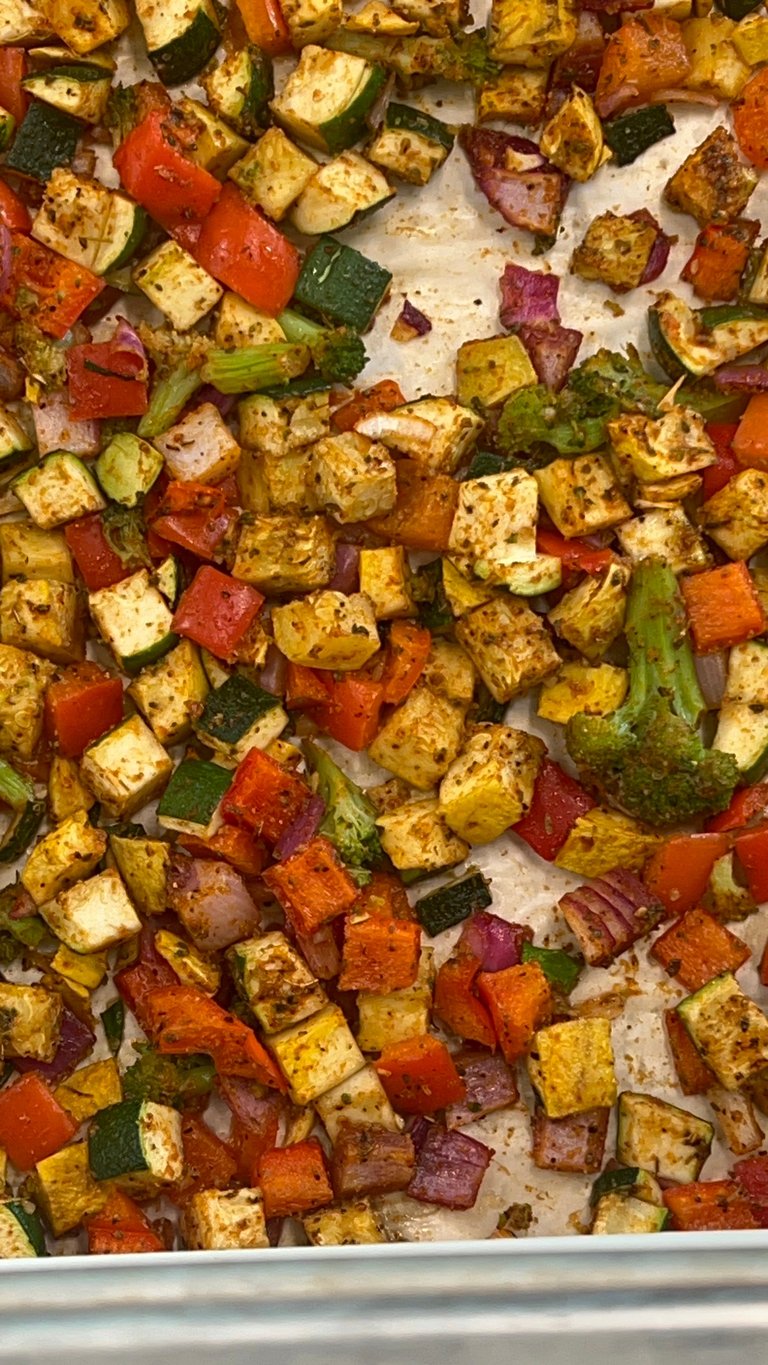 Roasted vegetables on parchment paper including cubed tofu, red peppers, zucchini, and green onions seasoned with herbs