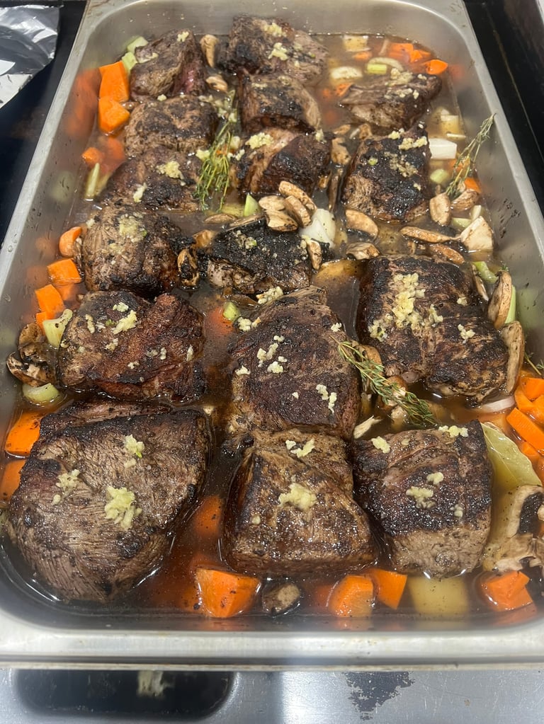 Seasoned beef steaks in a roasting pan with carrots, potatoes, and herbs, ready for cooking