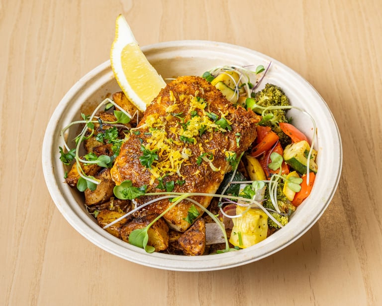 Seasoned crispy meat and roasted vegetables in white bowl with lemon wedge and microgreens on wooden surface